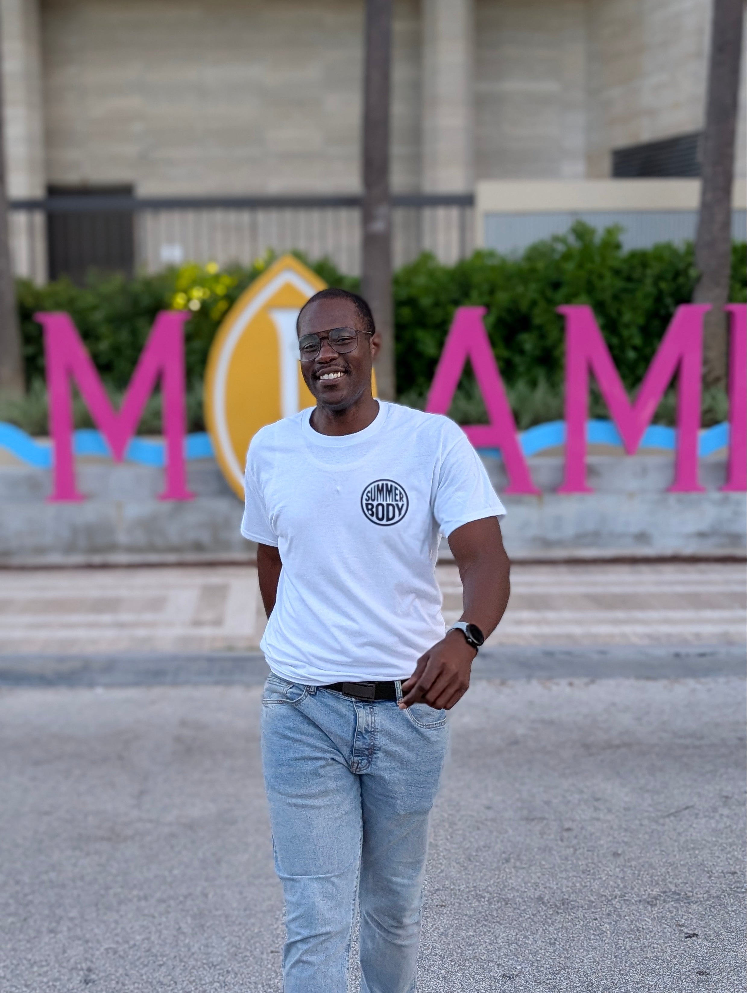 Man standing in front of a colorful 'Miami' sign with a building in the background